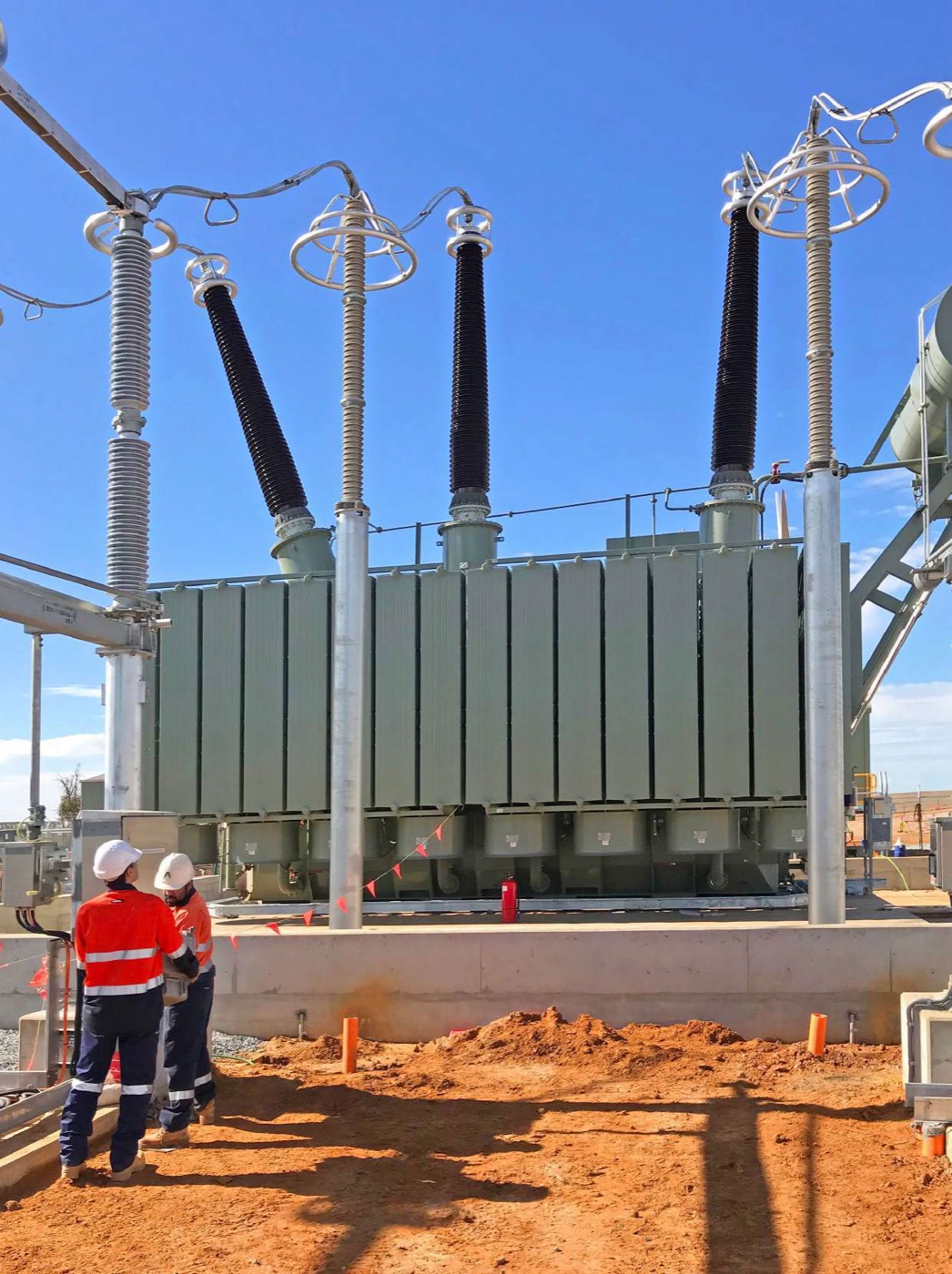 Two engineers inspecting a large power transformer with HV bushings