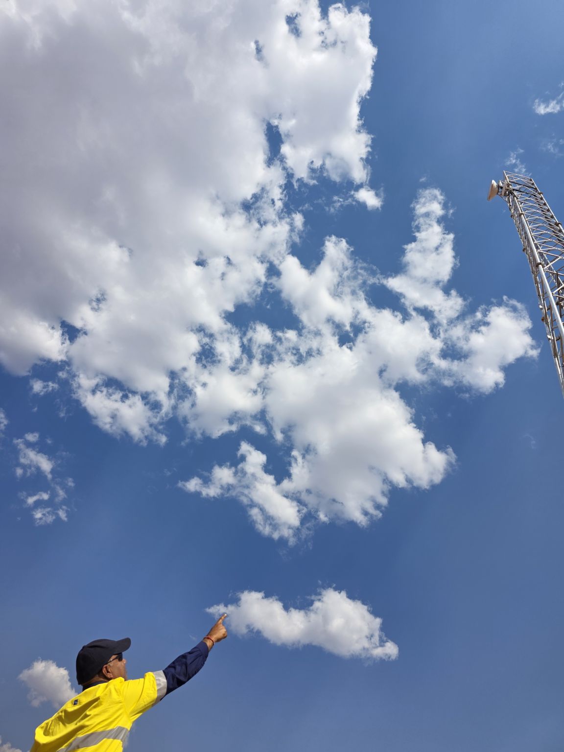APD Global field technician in hi-vis pointing up at a lattice communications tower with microwave dish on a remote site