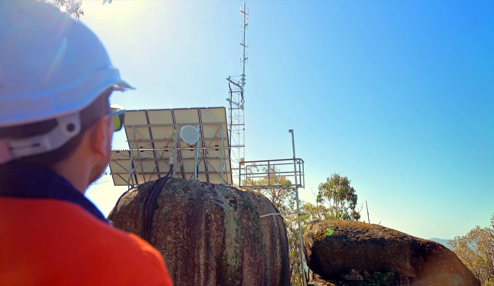 APD technician looking up at the solar-powered Mount Lawson emergency radio tower on its rocky outcrop
